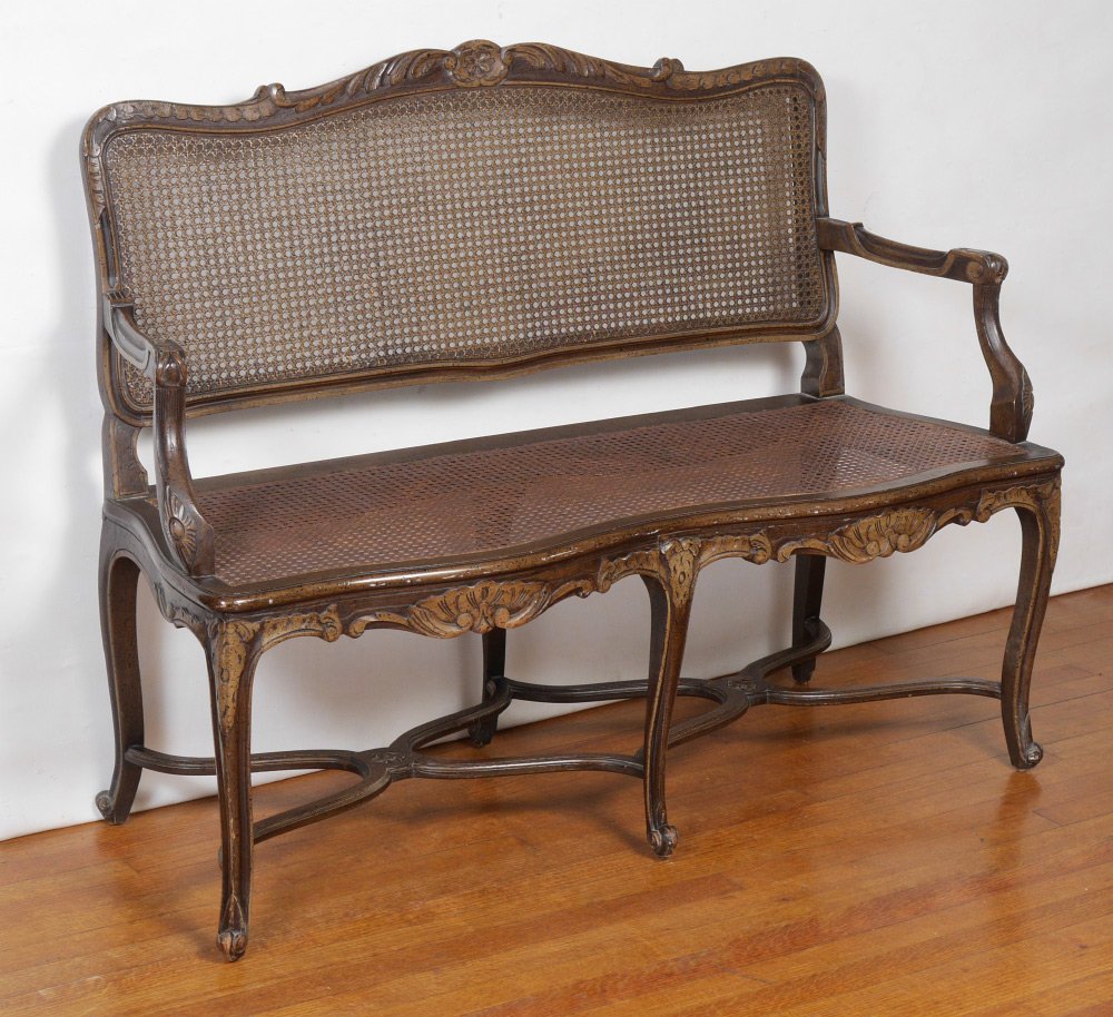 PROVINCIAL LOUIS XV STYLE SETTEE: PROVINCIAL LOUIS XV STYLE SETTEE: Early 20th century, the caned back surmounted by a foliate-carved crest and joined by scrolling arms, cane seat with foliate carved double apron on cabriole legs endi