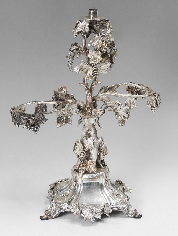 ORNATE SILVERPLATED EPERGNE: ORNATE SILVERPLATED EPERGNE: Grape vine motif with single candle top, openings for 2 inserts, flared base with applied grape vine motif. No visible mark, 20 1/4" h. x 15 3/4" x 10 3/4".
