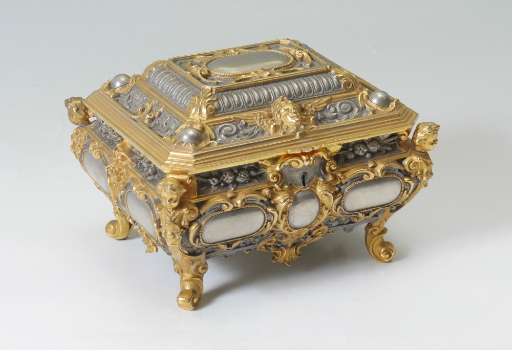 ROCOCO STYLE GILT METAL MUSICAL JEWELRY CASKET: ROCOCO STYLE GILT METAL MUSICAL JEWELRY CASKET: Mid 20th century production, silver and gold toned, hinged lid with cherub masquerons and foliate scroll. Body with figural putti busts at corners, addi