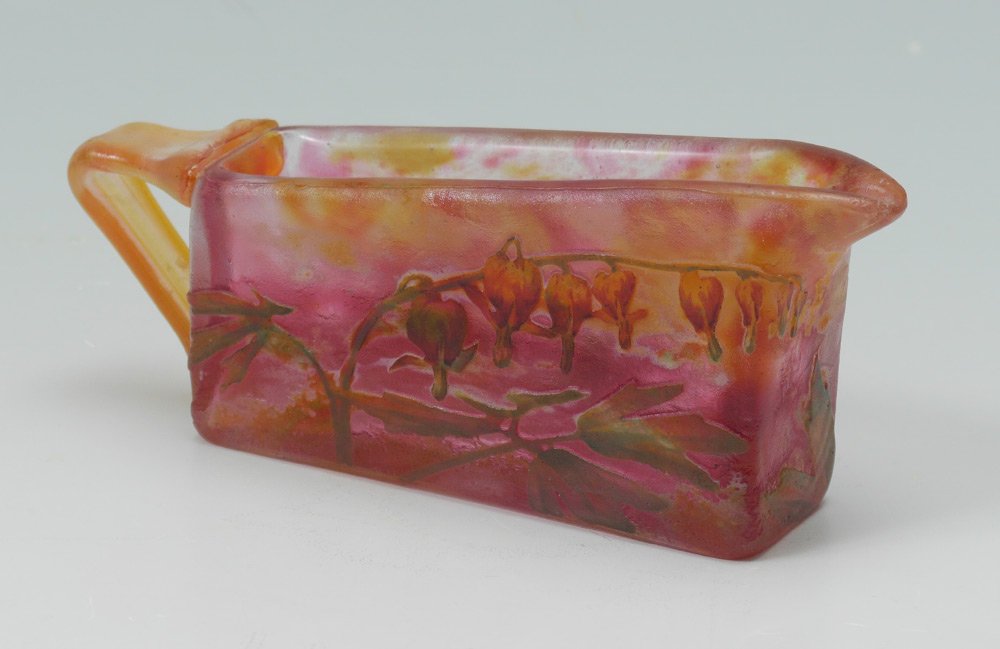 ATTRIBUTED DAUM NANCY CAMEO GLASS CREAM PITCHER: ATTRIBUTED DAUM NANCY CAMEO GLASS CREAM PITCHER: Cameo cut design of bleeding heart flowers on mottled fuchsia and orange ground. Unmarked attribution, 2'' h. x 5 1/8'' x 1 3/8''.