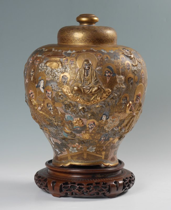 LARGE HODODA JAPANESE SATSUMA COVERED JAR: LARGE HODODA JAPANESE SATSUMA COVERED JAR: Ovoid for with gilt ground, enamel and high relief Buddhist figures, plants, dragons and animals, all on 3 shaped feet. Meiji or Taisho period, marked on bas