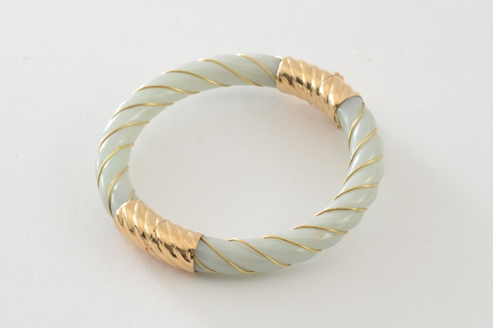14K GOLD AND JADE BANGLE BRACELET: JADE BANGLE BRACELET: 14K yellow gold and twist carved jadeite hinged bangle bracelet. Locking closure with safety chain. Diameter: 2.25" . Gold Weight: 4.0 grams approx.