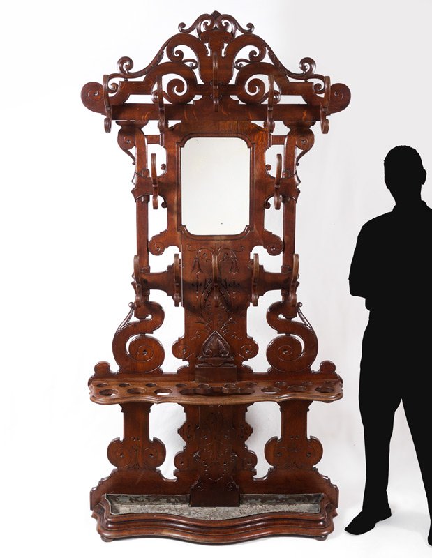 WALNUT VICTORIAN HALL TREE: WALNUT VICTORIAN HALL TREE: Open work scroll crest and body, 12 wood coat hooks, central mirror, carved decoration, open shelf with holes for umbrellas and walking sticks. Lower metal insert, overall 