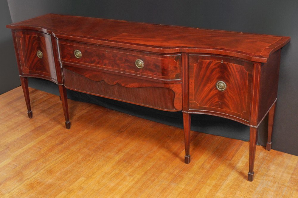 19TH CENTURY MAHOGANY SERPENTINE SIDEBOARD: 19TH CENTURY MAHOGANY SERPENTINE SIDEBOARD: Banded mahogany veneer serpentine top and front, 2 center drawers, right side with deep cellarette drawer, right side door with shelves. Tapered legs, overa