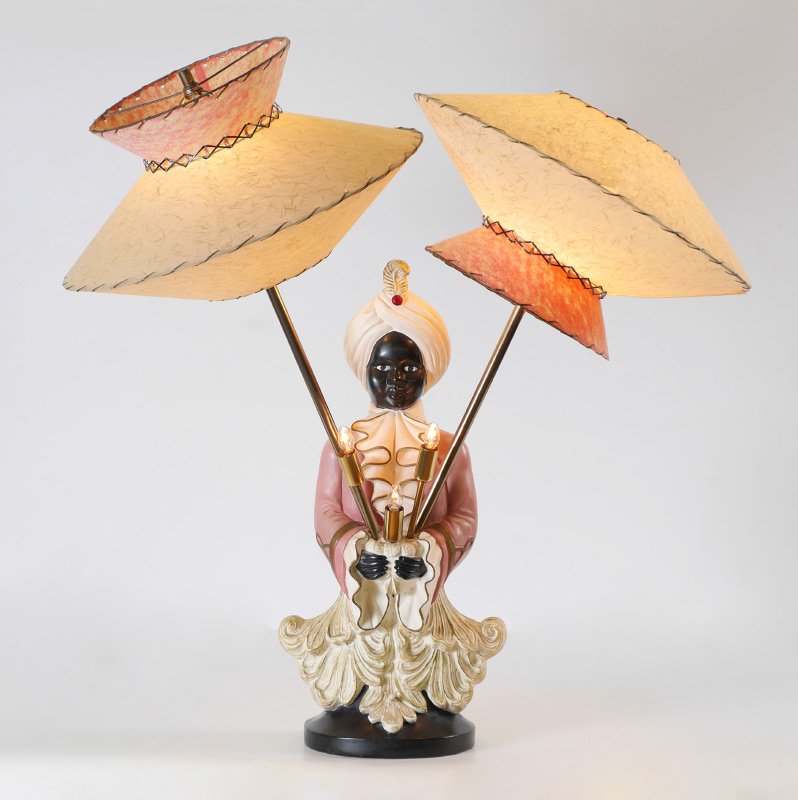 MID CENTURY BLACKAMOOR TABLE LAMP: MID CENTURY BLACKAMOOR TABLE LAMP: Ceramic figural bust of a blackamoor servant holding 5 lights total, 2 taller brass arms and 3 smaller in center. Multiple lighting options. No visible markings, lam