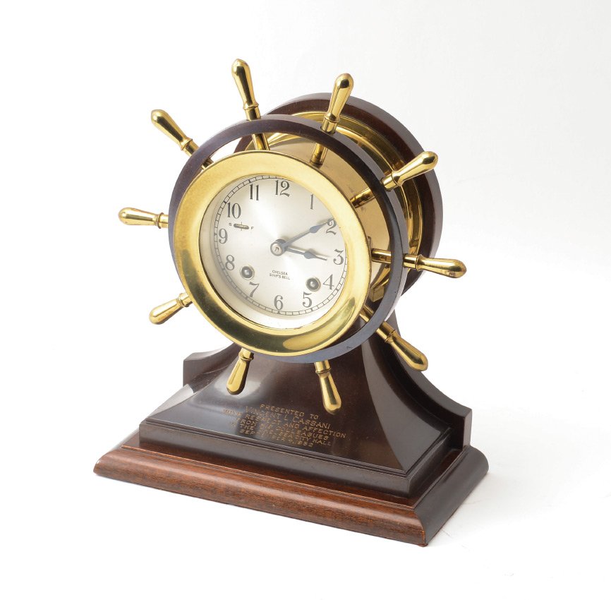 PRESENTED CHELSEA SHIPS BELL CLOCK: PRESENTED CHELSEA SHIPS BELL CLOCK: Brass ships wheel, bronzed metal stand, mahogany base silvered dial. Presentation on stand ''Presented to Vincent L Cassani with respect and affection from his coll