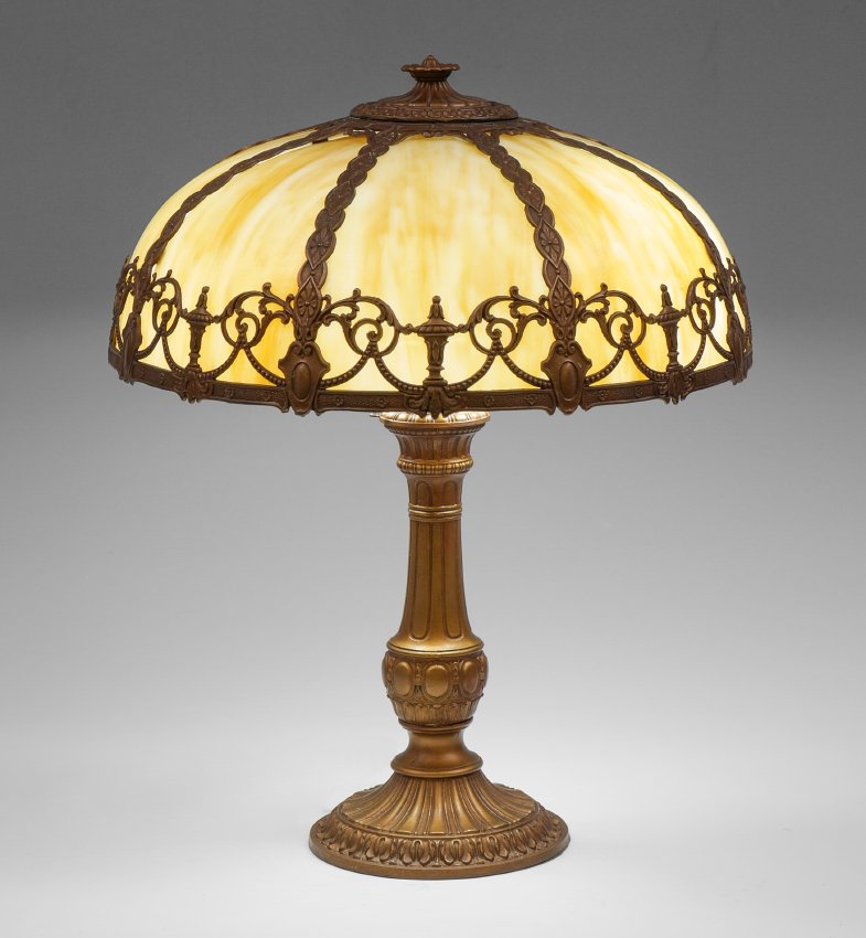 CARAMEL SLAG BENT PANEL LAMP: CARAMEL SLAG BENT PANEL LAMP: Ornate patinated cast metal base, double socket fixture, no visible markings, 22 3/4'' h. x 7 1/2''. Filigree frame 8 bent panel slag glass shade, 7 1/2'' h. x 18'' dia.