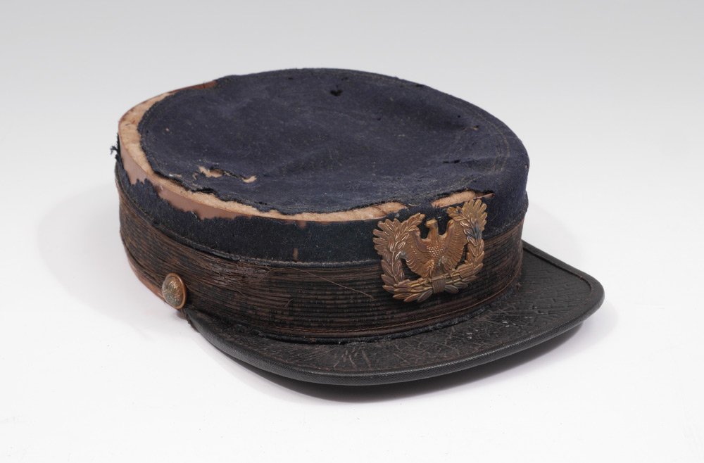 INDIAN WARS ERA US ARMY KEPI: INDIAN WARS ERA US ARMY KEPI: Circa 1870's blue cloth kepi, brass buttons and eagle hat badge, leather visor. Marked inside J. W. Calver & Son, 727 & 729 Arch St., Philada.. 2 1/4'' h. x 9 1/4'' x 6 1