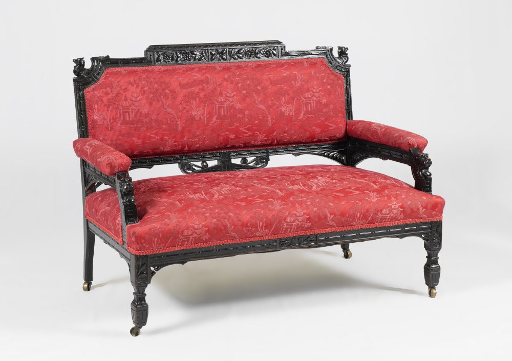 EBONIZED CARVED VICTORIAN SETTEE: EBONIZED CARVED VICTORIAN SETTEE: Ebonized carved frame, figural griffin at each end of top rail, lion masquerorns at arm supports, red oriental motif upholstery, all on castors. Measures 33 1/4'' h. 