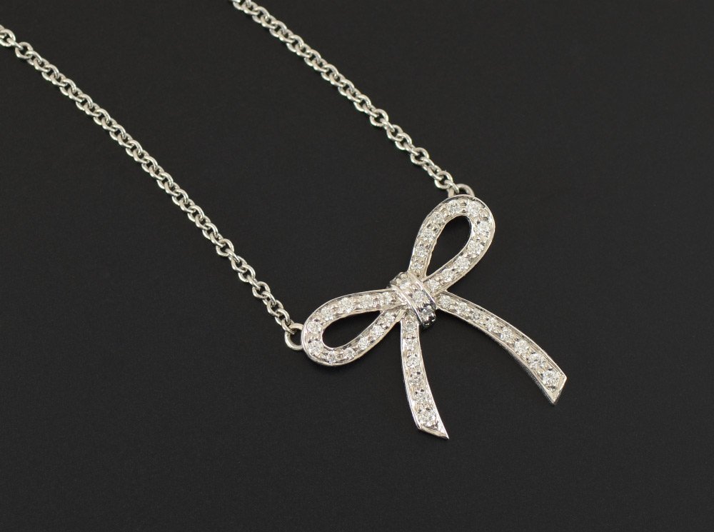 TIFFANY BOW TIE PLATINUM & DIAMOND PENDANT NECKLAC: TIFFANY BOW TIE PLATINUM & DIAMOND PENDANT NECKLACE: Platinum ''mini'' bow necklace contains 39 round brilliant cut diamonds. Weight: .11 CTW VS in clarity and G in color. Spring ring. Weight: 3.2 gra