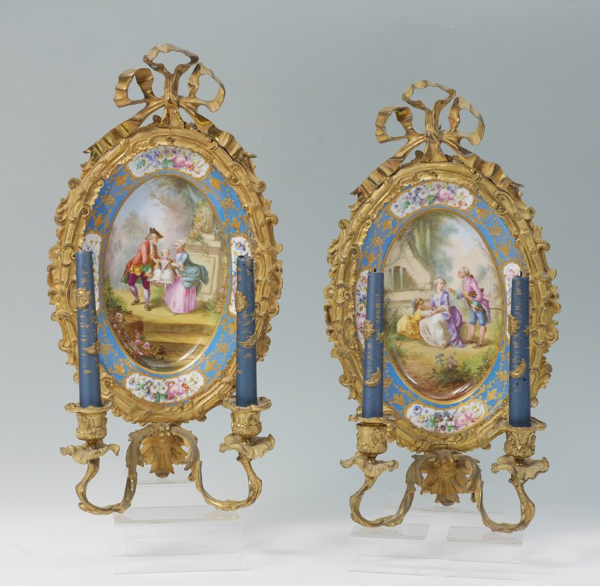 PAIR SEVRES STYLE PORCELAIN MOUNTED SCONCES: PAIR SEVRES STYLE PORCELAIN MOUNTED SCONCES: Hand painted oval porcelain plaques with genre scene center and floral decoration, gilt metal frames with ribbon finial, 2 arms each. Sevres style mark on 
