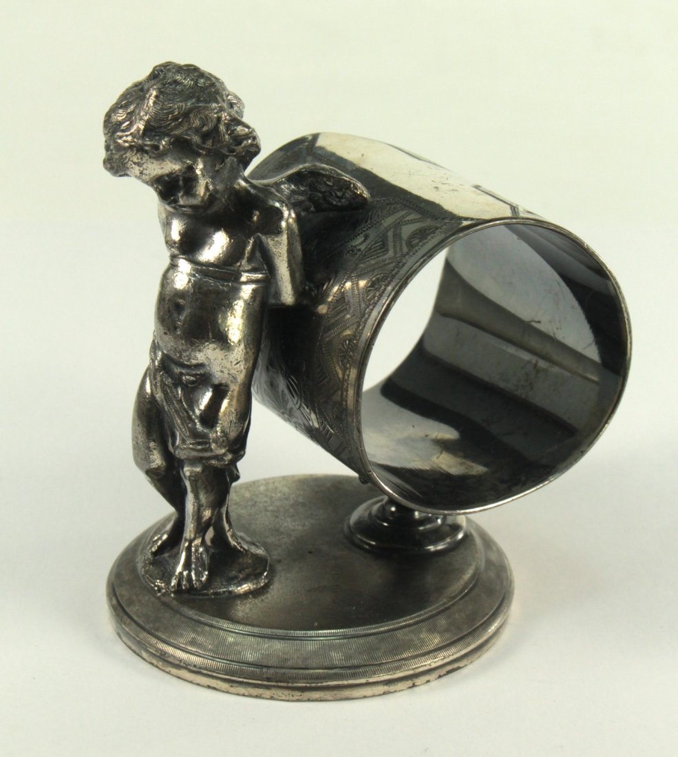 Antique Victorian JAMES J. W. TUFTS Boston Napkin Ring: Antique tabletop napkin ring in Victorian taste and of the period, made by James W. Tufts of Boston, Massachussetts. Displays a winged cherub, resting on a highly ornate ring and all on a circular ped