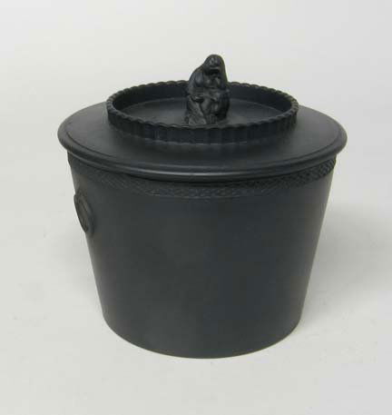 Black Basalt sugar box and cover, circa 1800, Po: Black Basalt sugar box and cover circa 1800 Possibly by Robert Wilson, the cylindrical tapered body with rouletted band to the top and molded ring handles, the cover with a crimped gallery and widow f