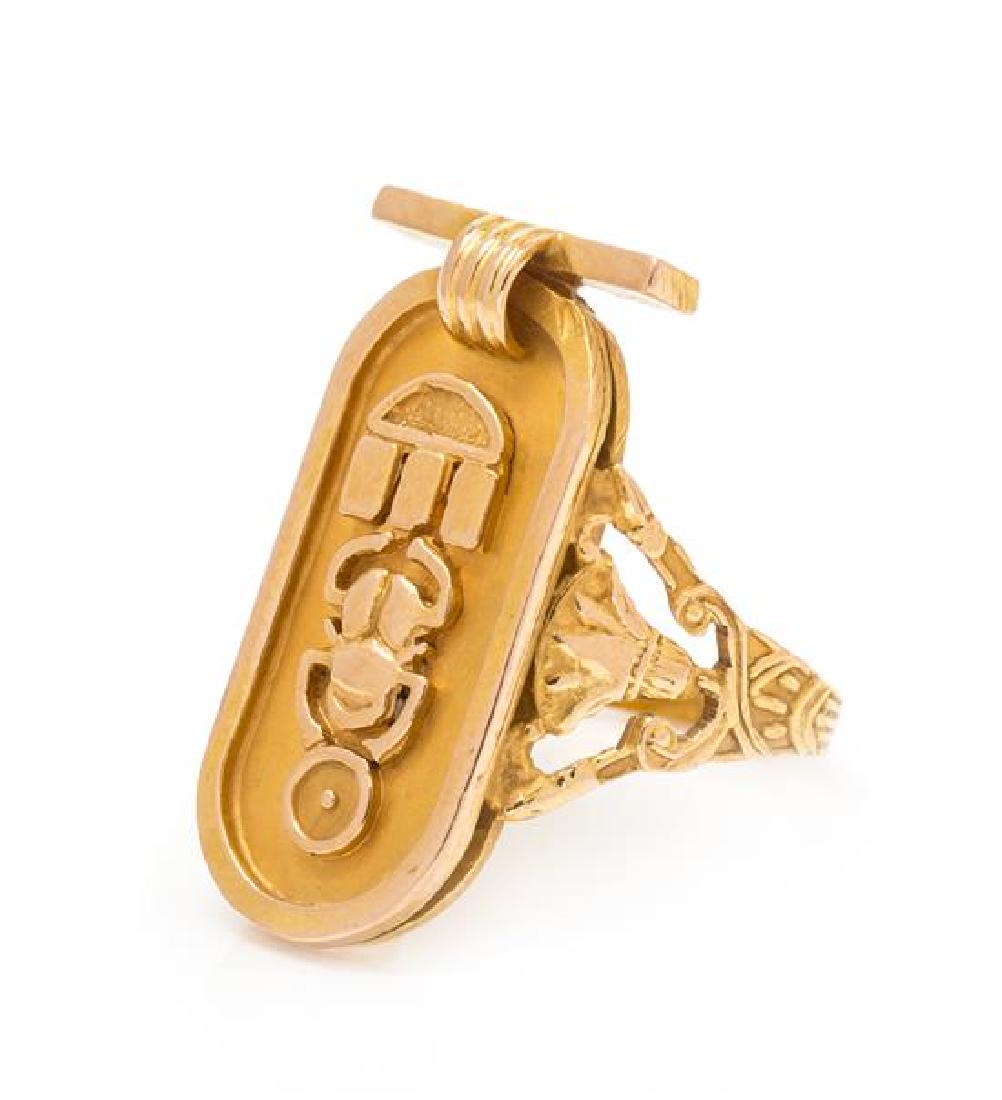 An 18 Karat Yellow Gold Egyptian Cartouche Ring, 3.00: An 18 Karat Yellow Gold Egyptian Cartouche Ring, with central cartouche with applied beetle and sun motif, and palmetto designs at the shoulders. Stamp: (Egyptian assay marks). 3.00 dwts. Estimate $ 2