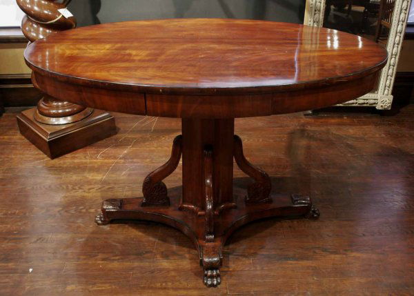 A Russian Neoclassical style mahogany centre table: A Russian Neoclassical style mahogany centre table oval top and columnar support with leaf-carved brackets on concave quatreform base upon paw feet 30 in. high, 48 in. wide, 30 ½ in. deep