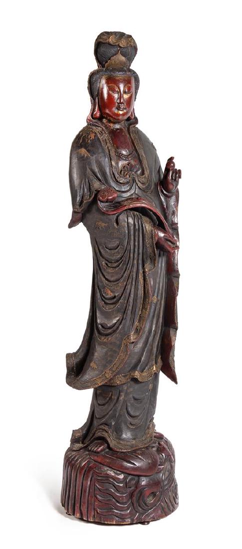 * A Large Carved Wood Figure of Guanyin Height 74 1/2: * A Large Carved Wood Figure of Guanyin 20th century the figure depicted standing on a circular base, the body slightly swayed to the side, wearing draped robes, the left hand bearing a pearl and the 