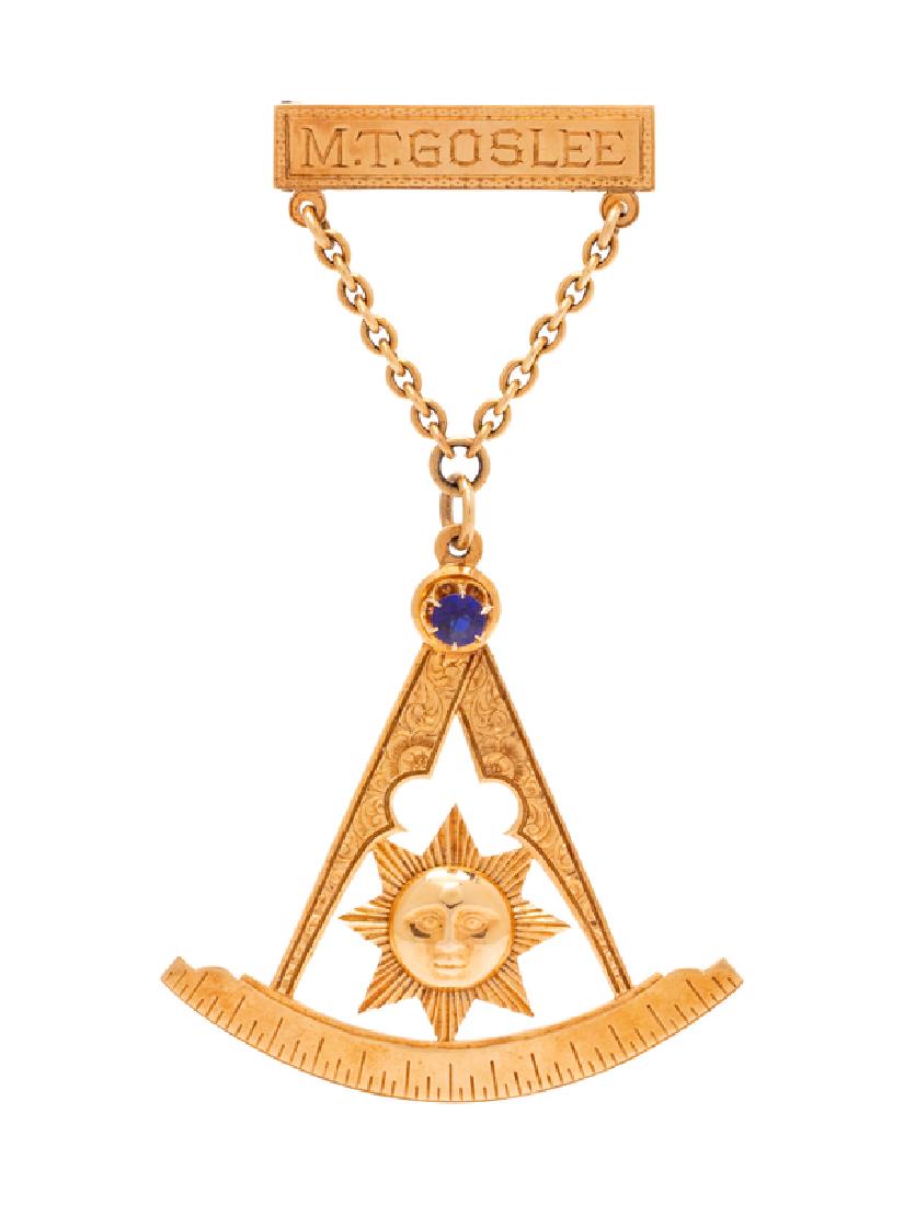An Antique Rose Gold and Synthetic Stone Masonic Lapel: consisting of a bar brooch engraved M.T. GOSLEE, with cable link chain suspending sundial motif pendant containing one round mixed cut blue synthetic gemstone. Reverse engraved: Presented by R. Fuller