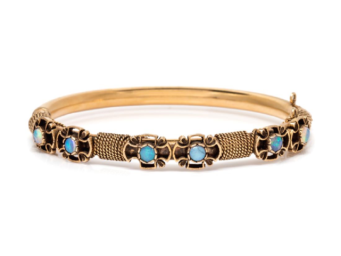 A 14 Karat Yellow Gold and Opal Bangle Bracelet,: containing six round cabochon cut opals measuring approximately 3.50 mm in diameter, with twisted gold wire detail, hinged with side clasp. Scratchmark: 14K. 11.05 dwts. Provenance: Property from the 