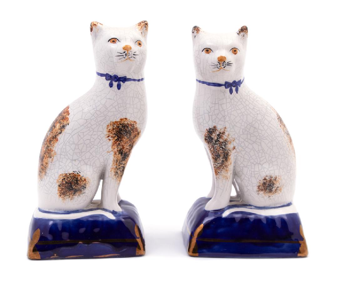 Pair of Staffordshire Earthenware Figures of Cats: 19TH CENTURY Each animal depicted with blue ribbon-tied collar, resting on a gilt-decorated cobalt-blue-glazed pillow. Height 7 1/2 x width 4 x depth 3 inches. Provenance: Property of an Atlanta Priva