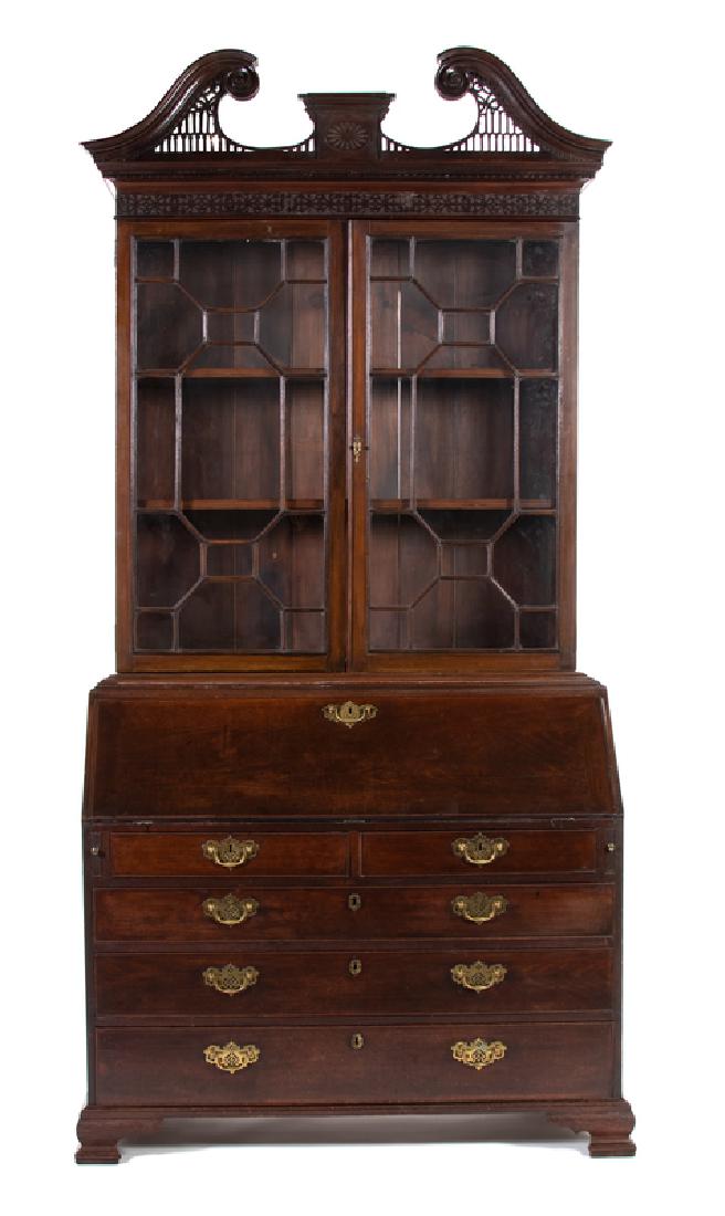*A George III Mahogany Secretary Bookcase: LATE 18TH CENTURY With swan's neck cresting above a blind fret-carved frieze over a pair of glazed doors enclosing two shelves, the lower section with a slant front enclosing an arrangement of drawers
