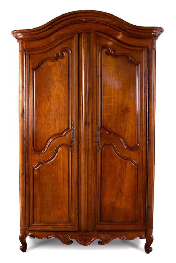 A Louis XV Provincial Carved Fruitwood Armoire : The molded cornice over two paneled doors opening to a plain interior, a scrolled apron below, raised on scroll-carved feet. Height 110 x width 65 x depth 25 inches.