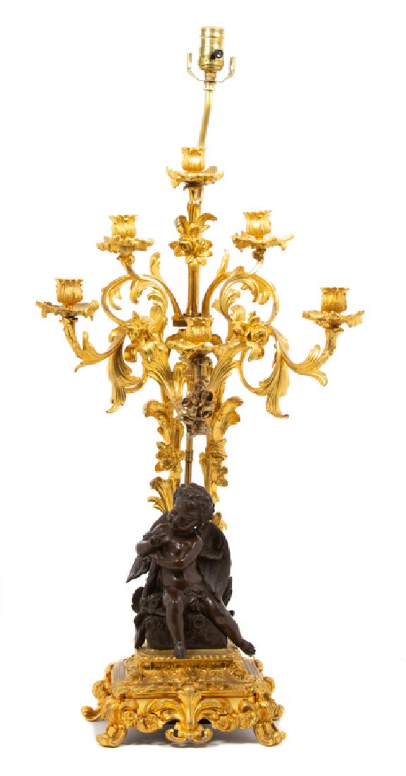 *A Louis XV Style Parcel-Gilt & Patinated Bronze: The six scrolling arms above a bronze figure of a seated putto on a plinth base, now wired as a lamp. Height of candelabrum 30 inches. Provenance: Property from the Collection of M. Anthony Greene, At