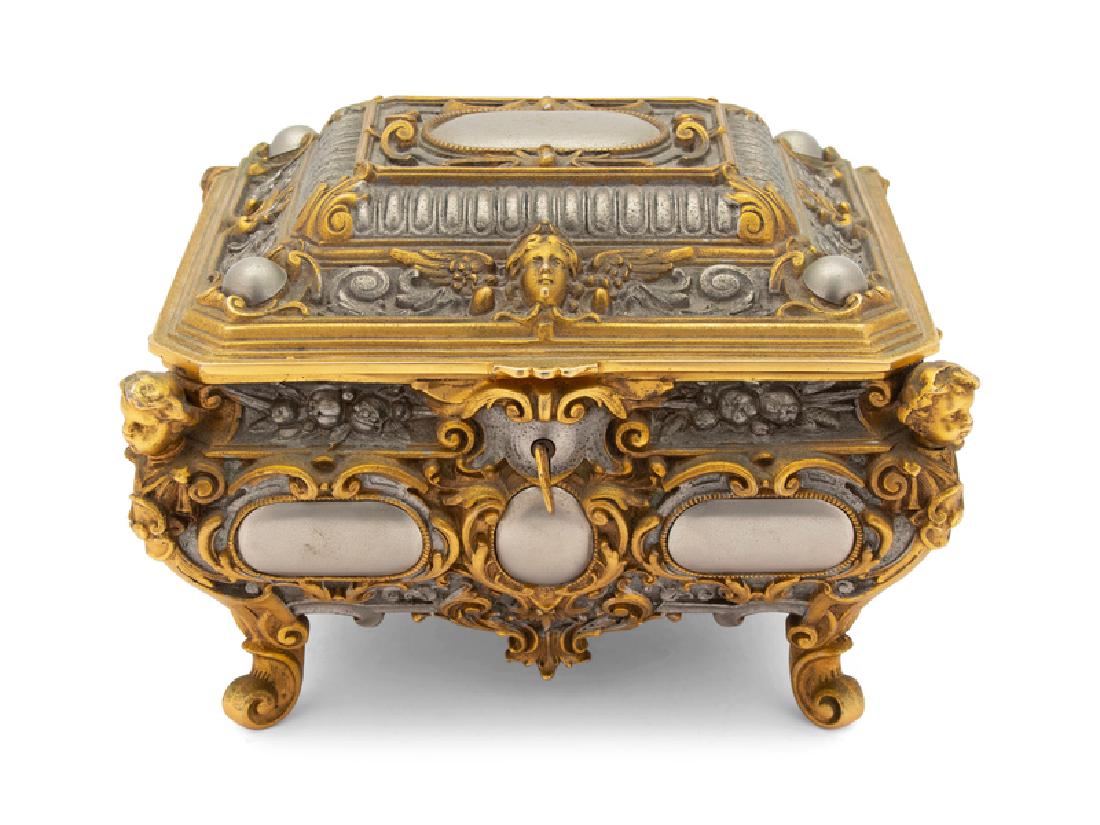 A French Belle Opaque Style Silvered and Gilt Metal: A French Belle Opaque Style Silvered and Gilt Metal Jewelry Casket 20TH CENTURY having corners mounted with cherub heads and scrolling foliage, opening to blue velvet interior, with working lock and k