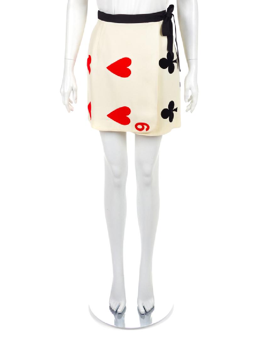 Moschino Wrap Skirt, 1990-2000s: Moschino Wrap Skirt, 1990-2000s White wrap skirt with a white playing card motif of a black 5 of Clubs on the left and a 6 of Hearts on the right. A black waistband wraps the skirt and ties on the sid