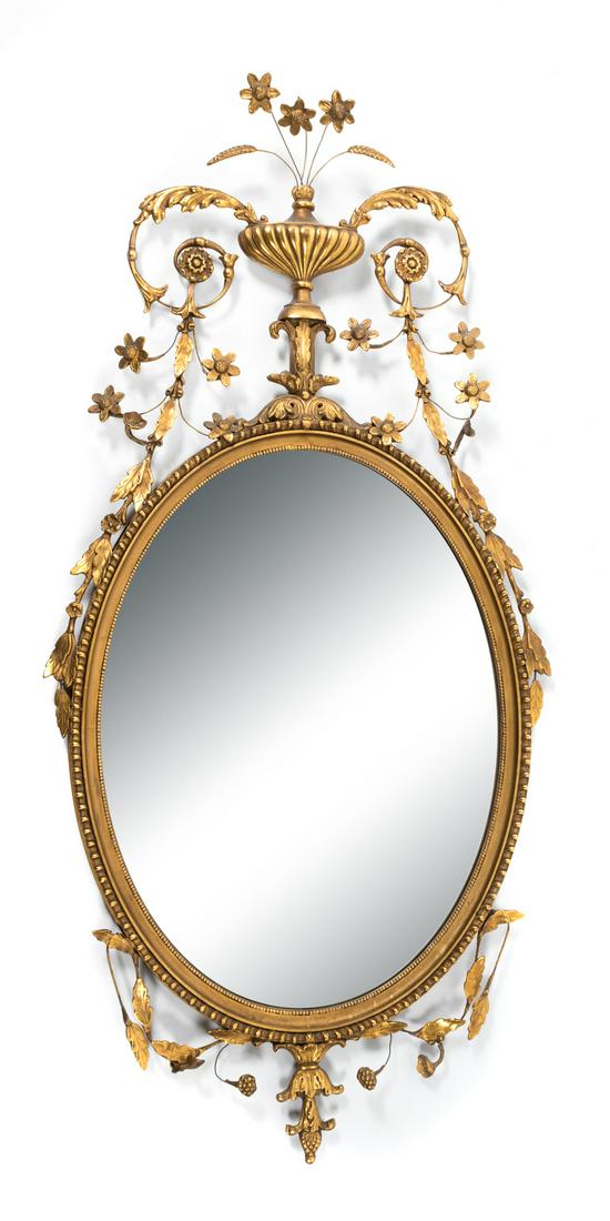 A George III Style Giltwood Mirror: A George III Style Giltwood Mirror The oval mirror plate within a beaded frame surmounted by a flower-filled urn with foliate trailings. Height 56 x width 27 1/2 inches.