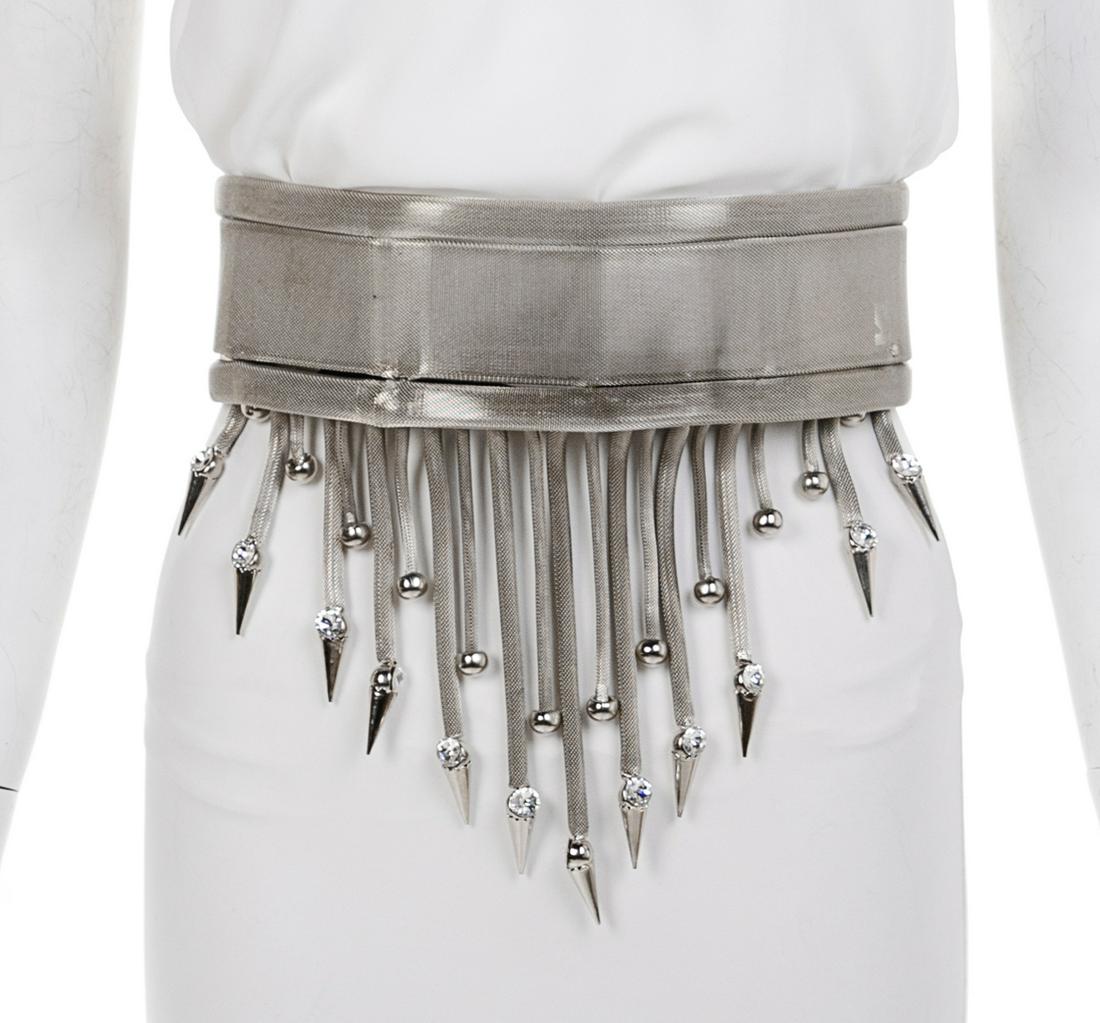 Versace Silvertone Mesh Belt with Fringe, 1990s: Versace Silvertone Mesh Belt with Fringe, 1990s Belt of wide band of silver mesh with metal grommets and hooks for the closure. Extending below the hem is metal fringe edged with metal balls and spike