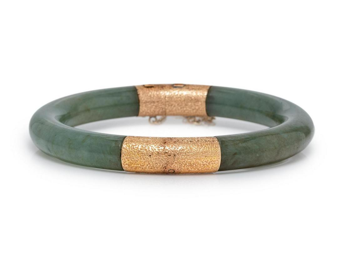 A 14 Karat Yellow Gold and Nephrite Jade Bangle: A 14 Karat Yellow Gold and Nephrite Jade Bangle Bracelet, consisting of two curved nephrite jade sections, hinged with side clasp and safety chain. Stamped: 14K Hong Kong. 24.10 dwts. Provenance: