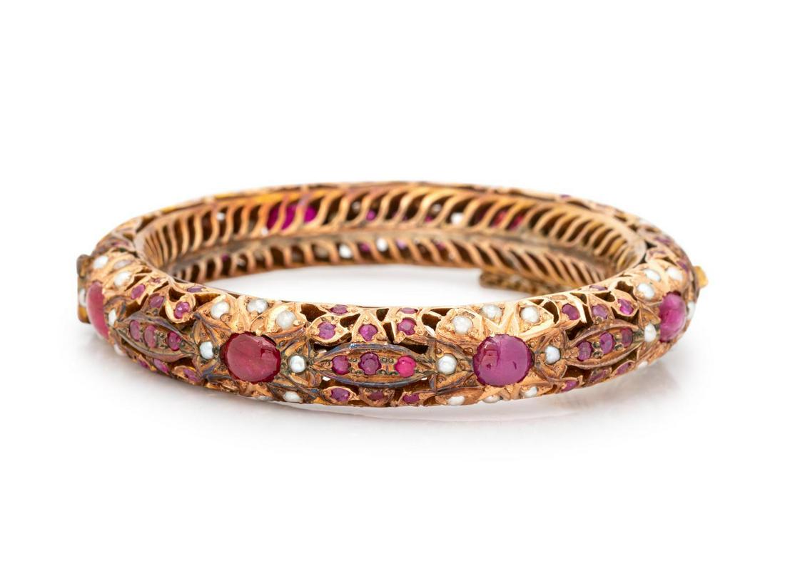 A 14 Karat Yellow Gold, Ruby and Cultured Pearl Bangle: A 14 Karat Yellow Gold, Ruby and Cultured Pearl Bangle Bracelet, containing numerous round and oval rubies and numerous pearls set in an open work design, hinged with side clasp and safety chain. St