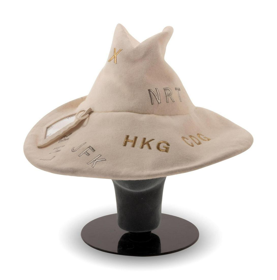 Stephen Jones Hat, 1990-2000s: Stephen Jones Hat, 1990-2000s Off-white felt hat with double pointed crown and wide bring. The hat is embroidered in goldtone and silvertone thread with airport name abbreviations. Label: Stephen Jone