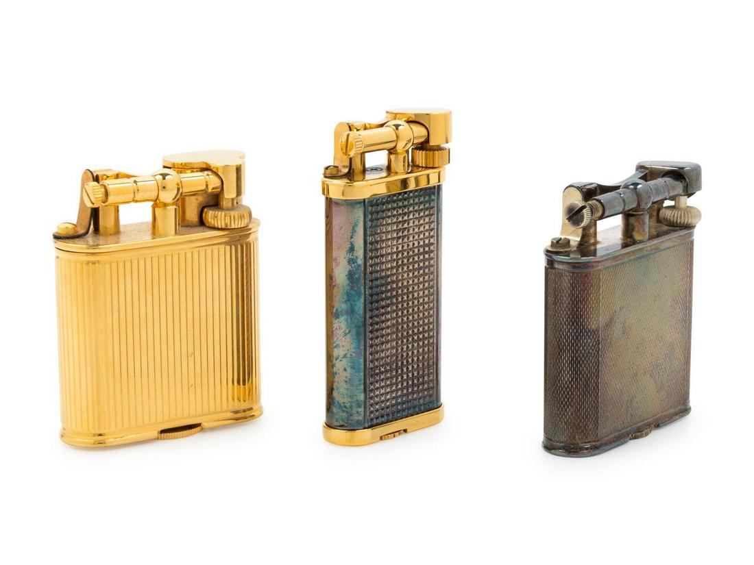 A Group of Three Dunhill Lift-Arm Lighters: A Group of Three Dunhill Lift-Arm Lighters 20th Century comprising a gilt metal example, a mixed metal example and a silver-plate example, the silver-plate example with a Dunhill retail box. Height