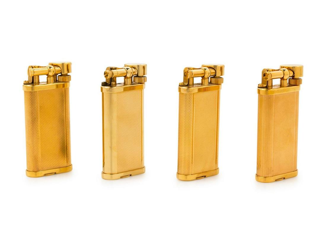 A Group of Four Gilt Metal Dunhill Lift-Arm Lighters: A Group of Four Gilt Metal Dunhill Lift-Arm Lighters three examples with an engine-turned case, the fourth example with a vertically reeded body. Height of tallest 2 1/2 inches. Property from a Mi