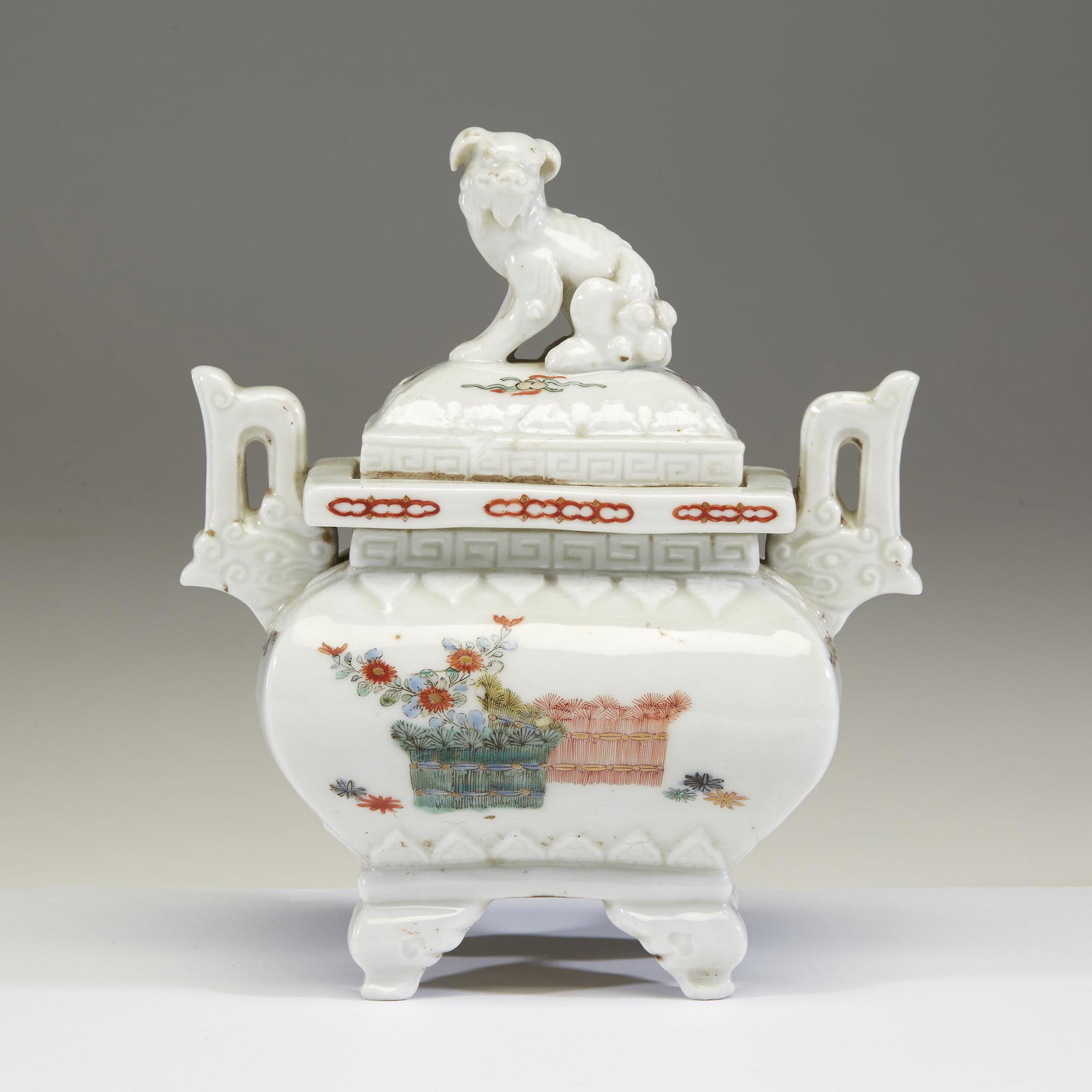 A Japanese enameled porcelain koro and cover, Edo: A Japanese enameled porcelain koro and cover. Edo period. Decorated in Kakiemon style, with archaic handles and cushion-form body balanced upon four legs, the cover topped with the figure of a kirin, 