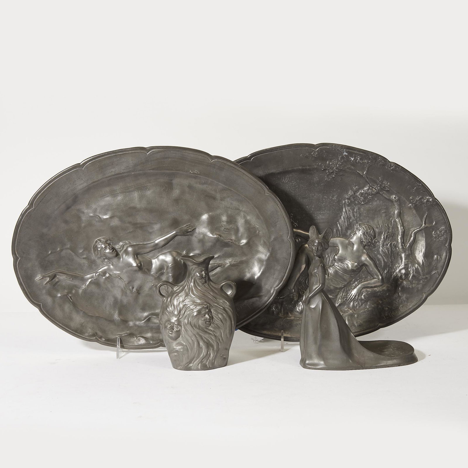 Kayserzinn (German, active 1862-1925), Collection of: Kayserzinn (German, active 1862-1925) Collection of four pewter wares, Germany, early 20th century. Comprising two oblong trays with relief reclining female nudes, a standing figure of a woman, and a 