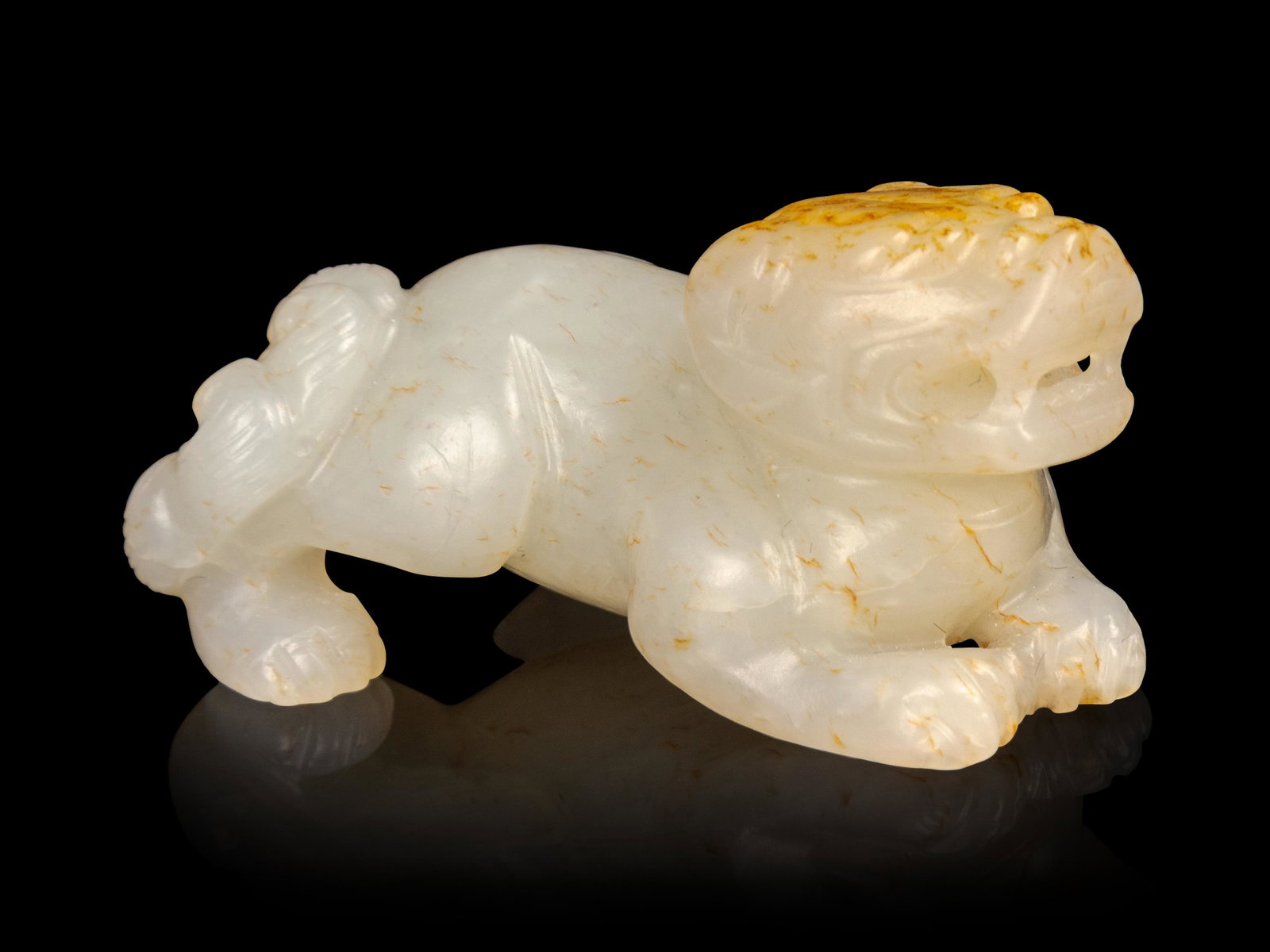 A Russet and White Jade Figure of a Recumbent Beast: A Russet and White Jade Figure of aÊRecumbent Beast carved recumbent with its head lifted and bearing its teeth, the stone of a very pale beige color. Length 2 1/4 in., 5.7 cm.
