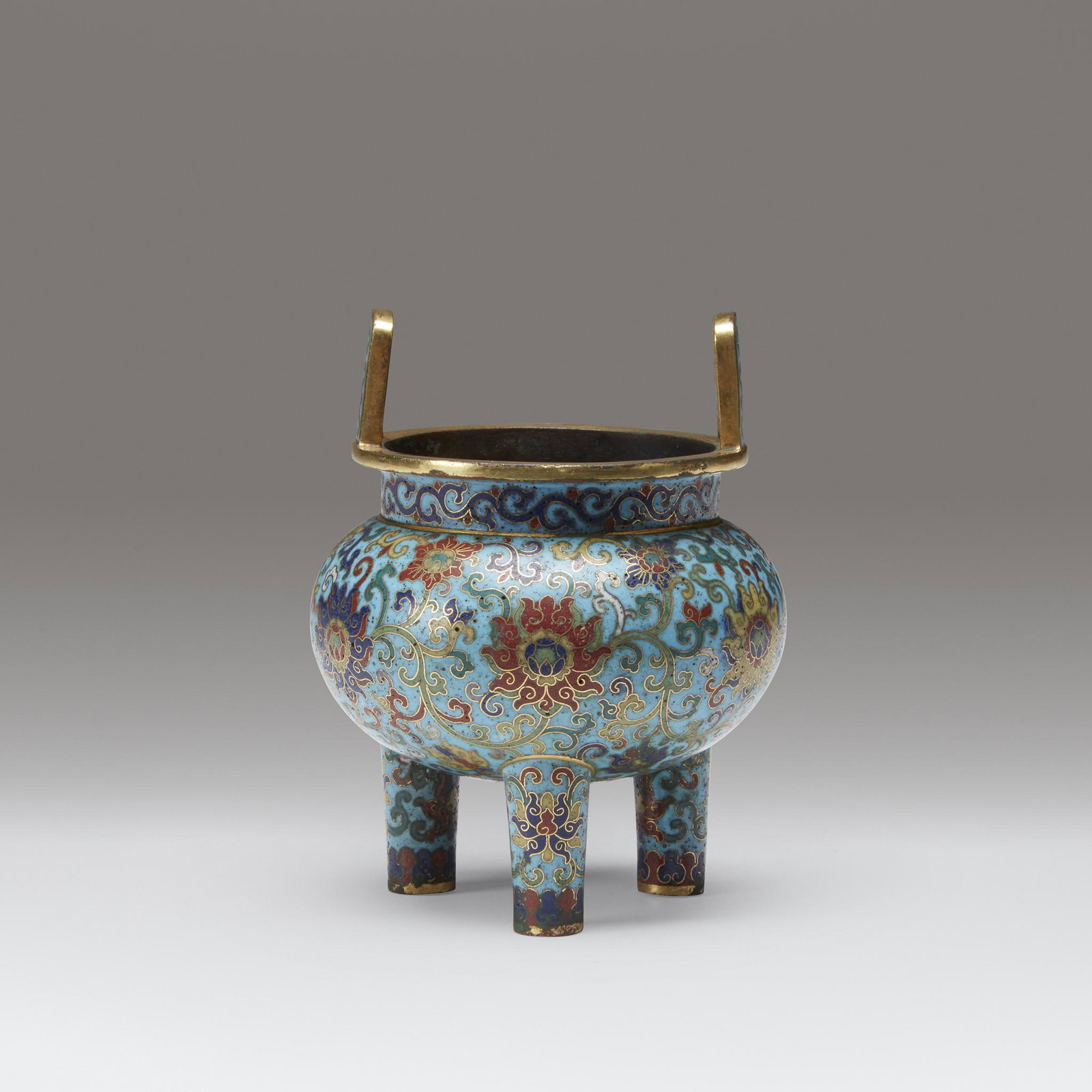 A Chinese cloisonné enamel tripod censer, Qianlong mark: A Chinese cloisonné enamel tripod censerQianlong mark and possibly of the periodThe compressed bulbous body with a pair of vertical bail handles, the body decorated with lotus scrolls, raised on thre
