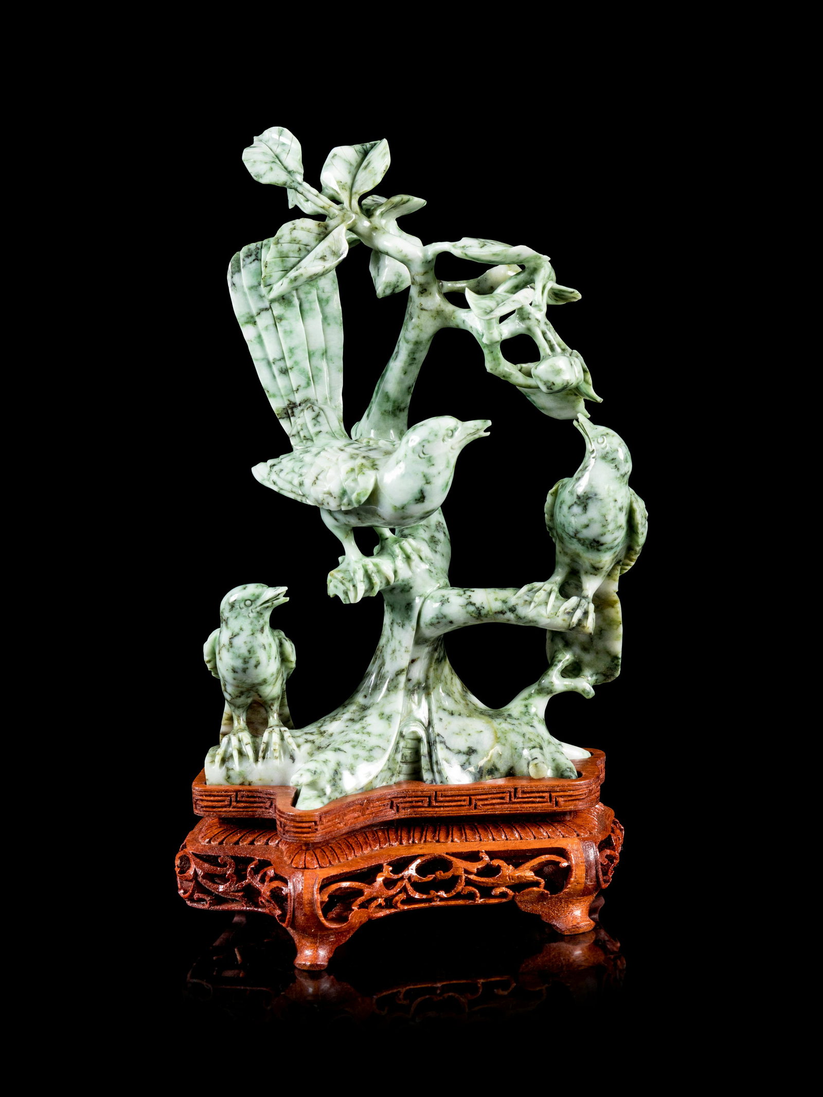 Two Chinese Green and Celadon Jadeite Figural Group of: Two Chinese Green and Celadon Jadeite Figural Group of Birds 20TH CENTURY each reticulated with birds perched on branches, supported on fitted wood stand. Height of taller 8 1/2 in., 21.5 cm. Property