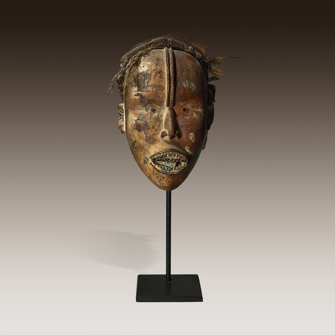 A Kongo mask: A Kongo maskDemocratic Republic of CongoLeather, fiber and glass, a leather hide stretched over a wooden frame, bound with vegetal fibers, the face presenting a fearsome visage, dual ridges run parall
