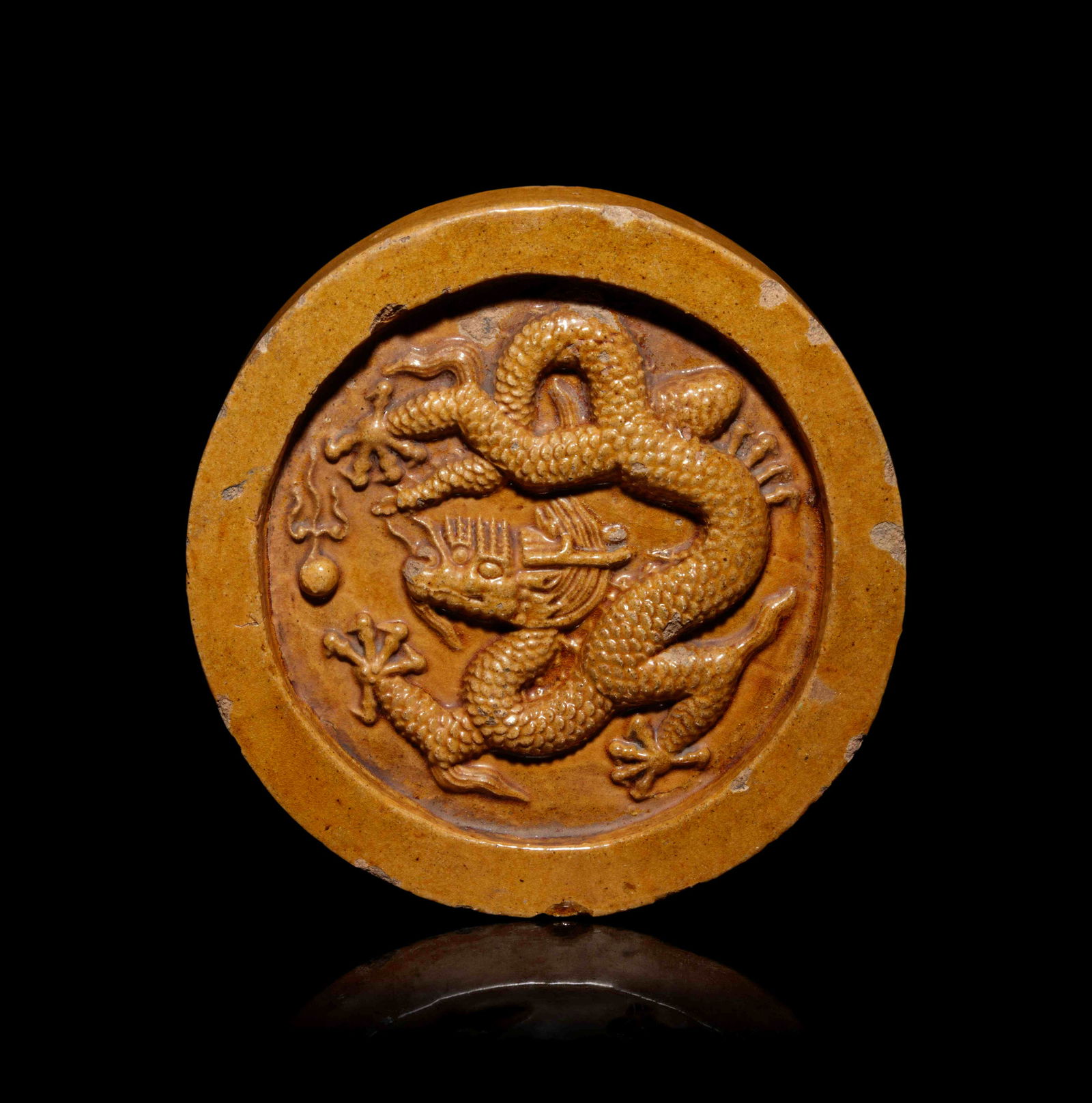 A Chinese Yellow Glazed ‘Dragon’ Roof Tile: A Chinese Yellow Glazed ‘Dragon’ Roof Tile of circular shape, moulded with a dragon chasing a flaming pearl, overall applied with amber yellow glaze. Diameter 7 3/4 in., 19.7 cm.