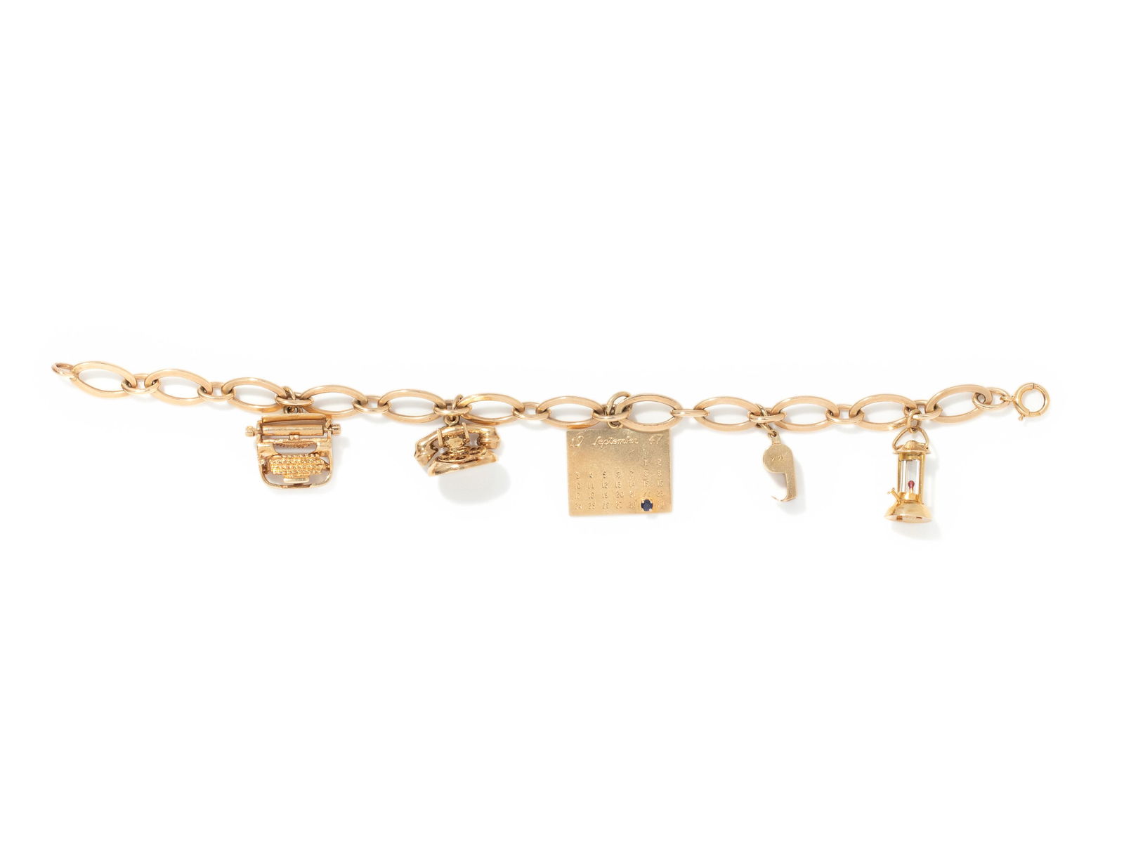 YELLOW GOLD CHARM BRACELET: YELLOW GOLD CHARM BRACELET Consisting of a fancy link bracelet suspending a typewriter charm, a telephone charm, a calendar charm with one sapphire marking September 29, 1947, a whistle charm and a la