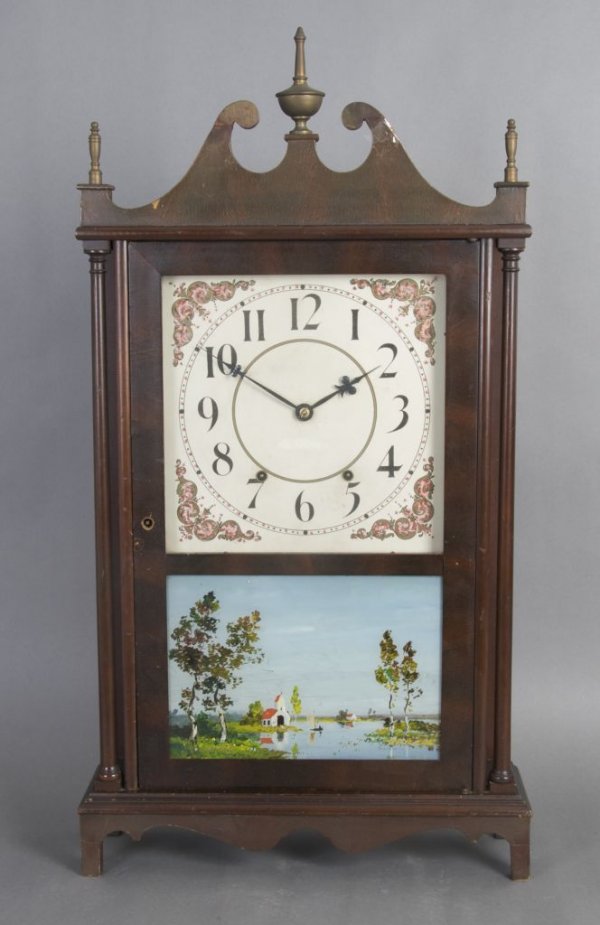 A Mahogany Wall Clock, Height 31 x width 17 1/4 x : A Mahogany Wall Clock, having a broken arch pediment and engaged columns above a carved apron, the dial having Arabic numerals set above a painted panel. Height 31 x width 17 1/4 x depth 5 inches.