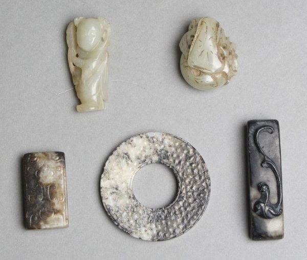 A Group of Five Chinese Jade Carvings, Width of widest : A Group of Five Chinese Jade Carvings, Han Dynasty and later, comprised of two chocolate brown, black and white stone sword fittings, one black and white carved bi disk and two celadon jade toggles, o