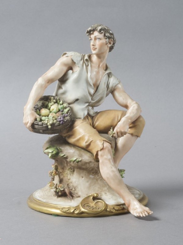 A Capodimonte Porcelain Figure, Height 8 1/4 inche: A Capodimonte Porcelain Figure, depicting a seated man holding a basket of fruit and flowers, marked 'Cappe' to base. Height 8 1/4 inches.