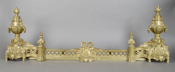 A Pair of Louis XVI Style Gilt Metal Chenets, Height of: A Pair of Louis XVI Style Gilt Metal Chenets, each with flaming urn form finial, joined by a ribbon centered fender. Height of pair 13 1/2 inches.