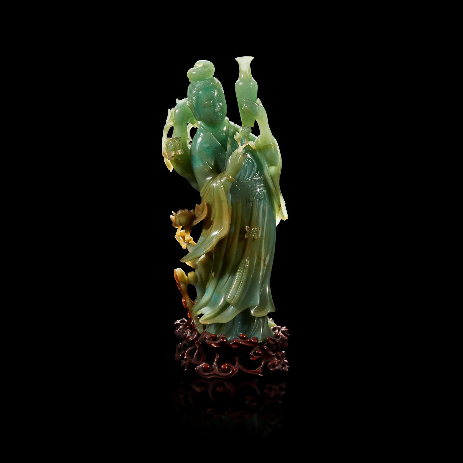 A Chinese carved jadeite meiren: Depicted draped in a flowing robe, fluttering at the sleeves and hem, her hair pulled into a high chignon, delicately bearing a slender baluster vase, in front of a phoenix perched atop a blossoming s