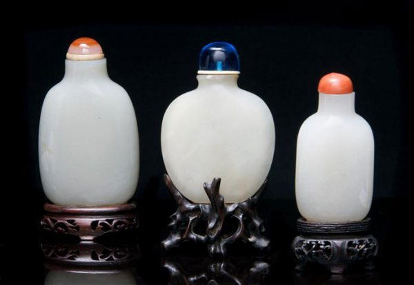 A Group of Three Jade Snuff Bottles, Height of tal: A Group of Three Jade Snuff Bottles, the first of compressed flask form, of mutton fat colored stone with blue glass stopper and having fitted root form wood stand, the second of transparent white sto