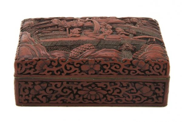 A Chinese Cinnabar Lacquer Lidded Box, Width 5 1/2: A Chinese Cinnabar Lacquer Lidded Box, having a figural scene on the lid, the side with scrolling foliate decoration, having gold tone six character Qing reign mark on underside. Width 5 1/2 inches.